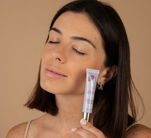 Woman holding Makari Retinol Control Line Smoothing Eye Cream against a beige background