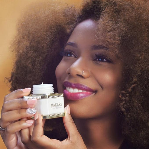 Woman holding a Makari De Suisse Night Radiance Treatment Cream with a warm background