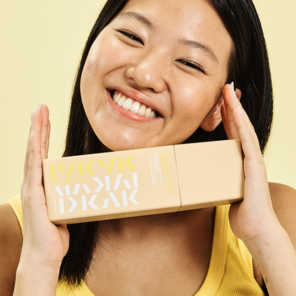 Woman holding Makari IYKYK Ceramide Collagen + Peptides Body Toning Cream against a yellow background