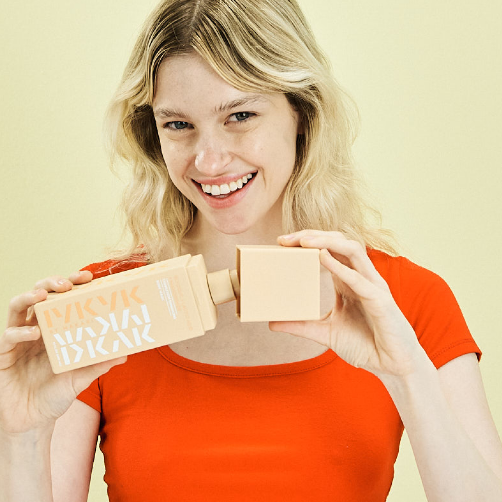 Woman holding Makari IYKYK Glycolic + Lactic Acid + Niacinamide Body Washwith a plain background