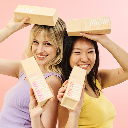 Two women holding makeup boxes on a pink background