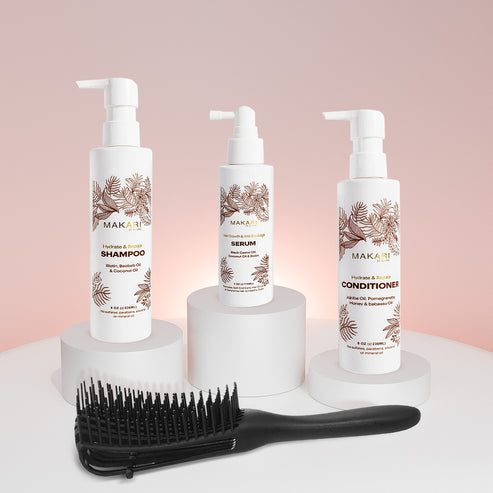 Makari Hydrate & Repair Haircare Set including shampoo, serum, and conditioner with a hairbrush on a light pink background.