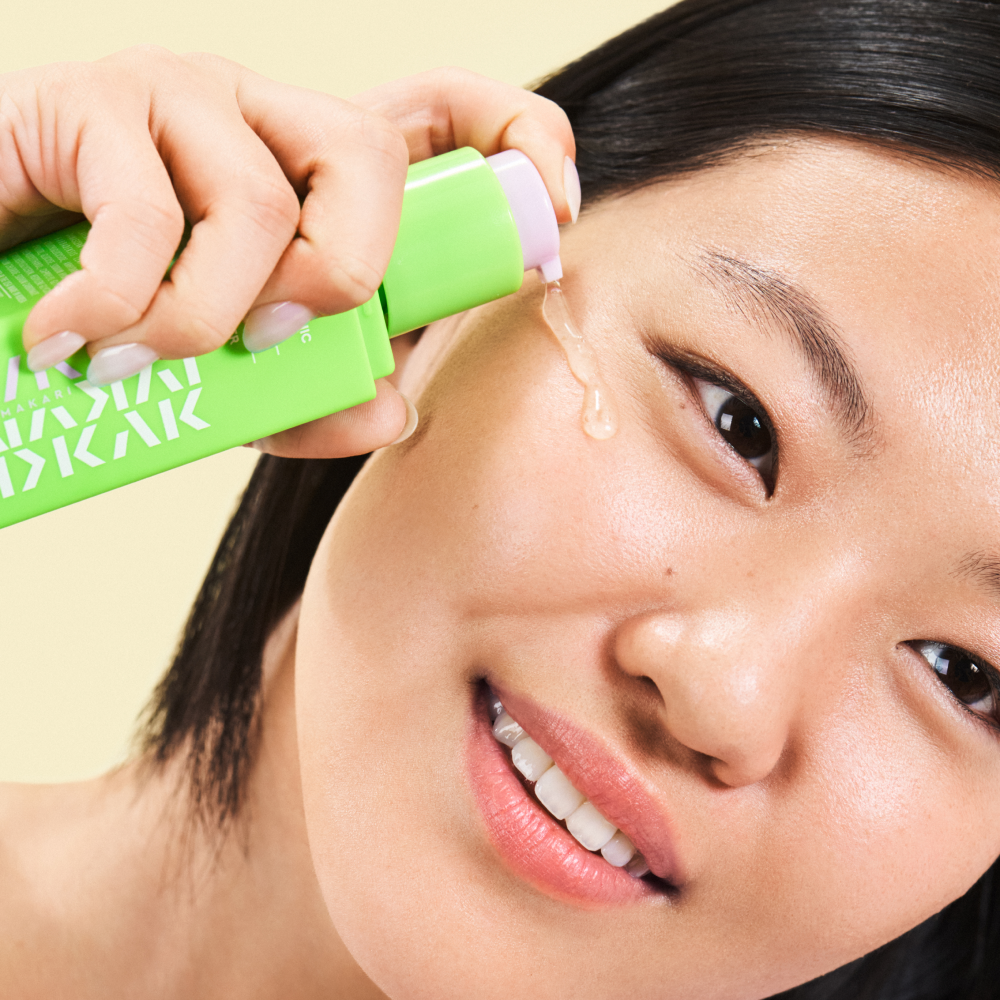 Person using Makari IYKYK Hyaluronic Acid 2% Hydration Booster on their face with a yellow background