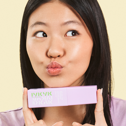 Woman holding a pink IYKIK box with a playful expression against a yellow background