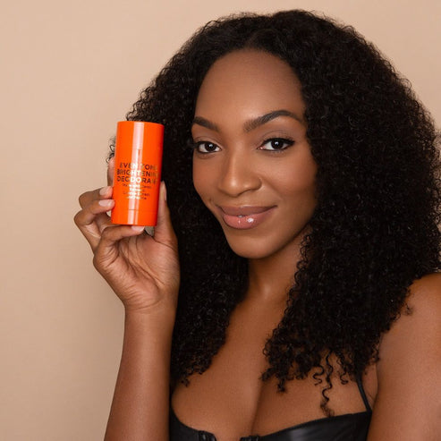 Woman holding Makari Even Tone & Brightening Deodorant Stick against a beige background