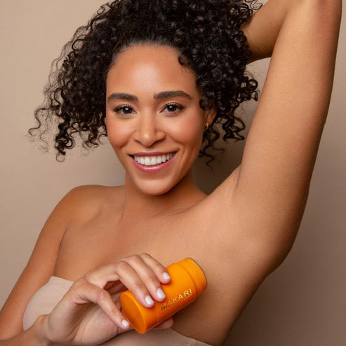 Woman applying Makari Even Tone & Brightening Deodorant Stick to her armpit against a beige background
